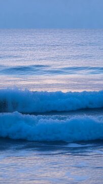 Vertical video: Incoming swell driving waves curling and breaking nearshore forming whitewater foam