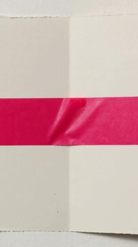 Vertical video: Camera filming cream folded paper on table while light shifting revealing red tape
