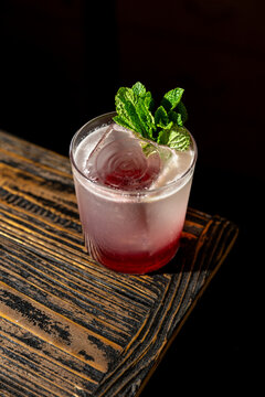 This drink has mint leaves and ice, sitting on a wooden table in a dim area during the afternoon
