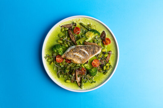 Fresh fish dish with green sauce and vegetables on a blue background for a modern dining experience in a restaurant setting