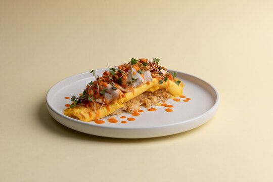 Omelette with rice served on plate with sauces and fresh herbs at a restaurant in daylight