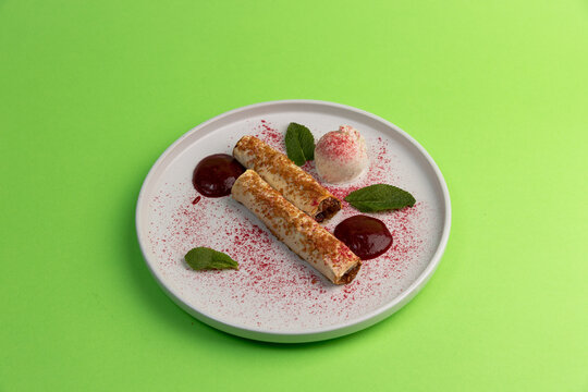 Dessert plate with rolls, sauce, mint, and ice cream on a green table during a bright day