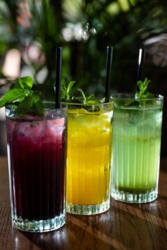 Group of colorful drinks sitting on a wooden table in a garden during a sunny afternoon