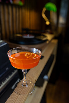 Cocktail served on a wooden table next to a turntable in a bar during evening hours