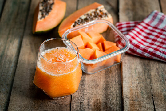 Fresh papaya juice in glass with sliced and cubed papaya on rustic wooden table healthy tropical fruit refreshing drink composition
