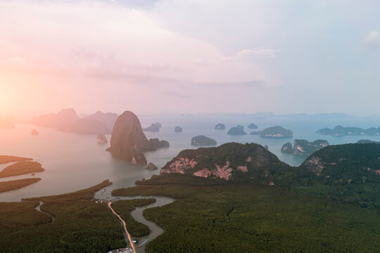 View from above: Majestic limestone formations rise above emerald waters fringed by winding mangroves, with a bustling coastal village visible at sunset.