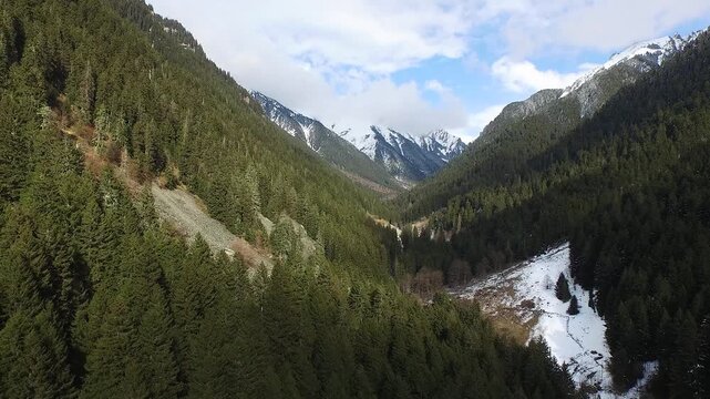 Aerial flight above green forest valley with mountains on horizon during early spring season. Snow patches remain slopes creating cinematic New Zealand alpine wilderness mood.