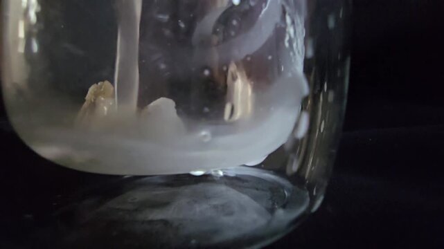 A piece of frankincense in a glass jar, covered with an infusion. More infusion is slowly poured over it, creating a captivating display of natural resin extraction and blending.