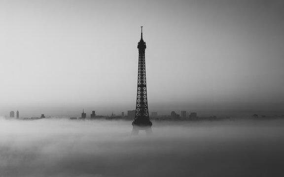 Tall oil derrick standing in a foggy field during the day with industry