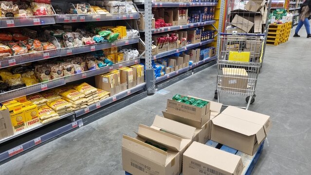Supermarket aisle restocking with cardboard boxes and shopping cart in retail store