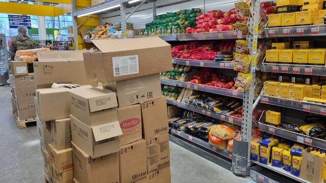 Supermarket restocking process with stacked boxes in grocery aisle and food shelves