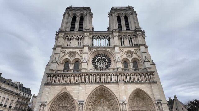 Tilt-down reveal shot of the Notre-Dame de Paris Cathedral facade under a cloudy sky.