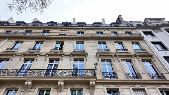 Low angle static shot of a classic Haussmann-style building facade with ornate wrought iron balconies and stone detailing.