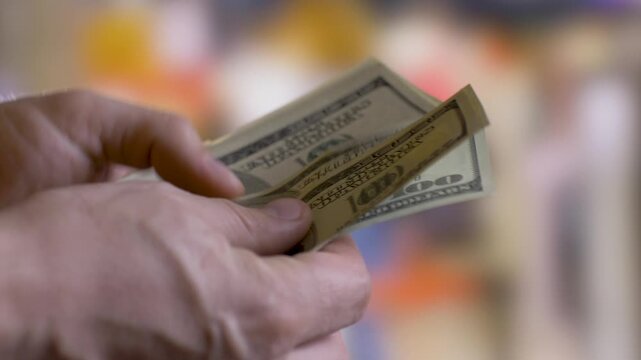 Person holding and counting us dollar bills in denomination of 100 slowly, one by one in hands. Close-up. Blurred background. Financial aid concept