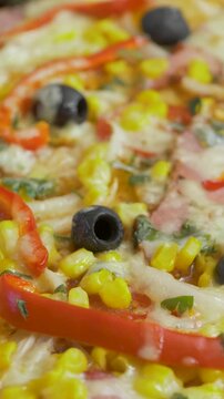 Newly baked pizza presents corn, pepper, onion, ham, olive, herb detail beneath soft cheese. Deep flavor dish at home kitchen