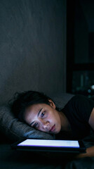 Obraz premium Insomniac woman stares at tablet in dark bedroom at night