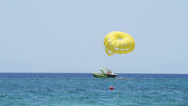 Parasailing adventure on blue sea with yellow parachute pulled by green motorboat during summer day.