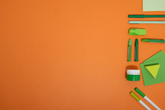 Bright orange background with green stationery items arranged with copy space, ideal for creative school and design concepts.