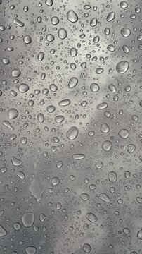 Raindrops dripping onto panoramic glass from above, close-up