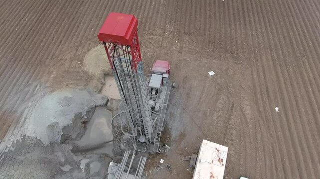 Aerial view of a drilling rig extracting groundwater from a flat alluvial plain farmland. Infrastructure, underground, engineering, and freshwater show industrial process and heavy operations.