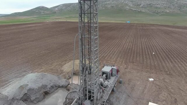 Aerial view of a drilling rig extracting groundwater from a flat alluvial plain farmland. Infrastructure, underground, engineering, and freshwater show industrial process and heavy operations.