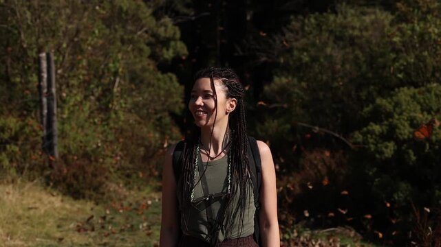 A young woman stands in a Mexican forest surrounded by thousands of monarch butterflies, watching in awe. At sunset, they drift around her, settle on trees and leaves, and fill the air with quiet