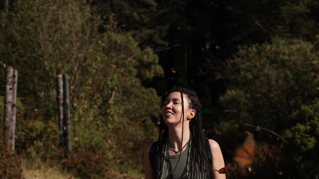 A young woman stands in a Mexican forest surrounded by thousands of monarch butterflies, watching in awe. At sunset, they drift around her, settle on trees and leaves, and fill the air with quiet
