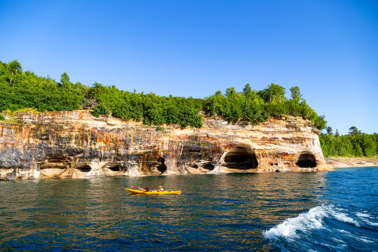 Kayakers explore the base of the towering, mineral-stained sandstone cliffs and sea caves along the vibrant shoreline of Pictured Rocks National Lakeshore in Michigan.