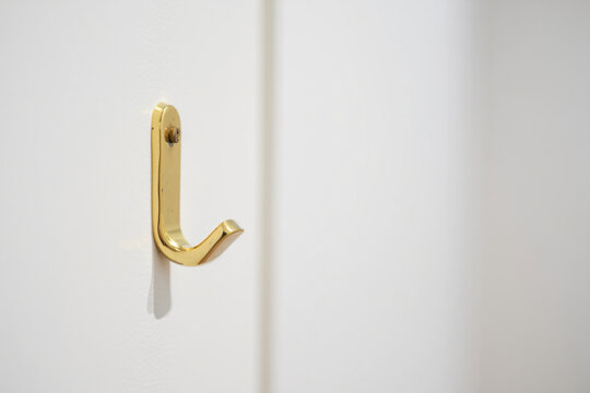 A small, polished brass hook mounted on a white wall, offering a touch of elegant hardware and practical functionality in a minimalist interior.