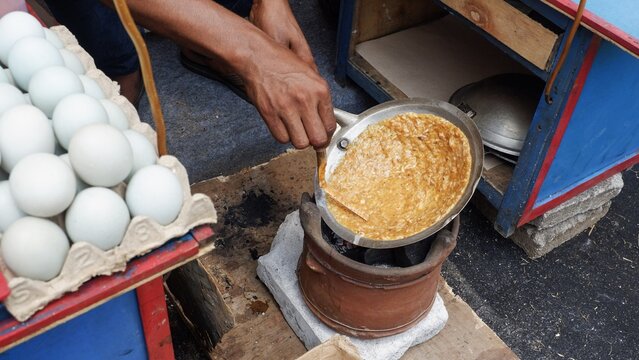 A street food vendor cooking Kerak Telor, a traditional Betawi spicy omelet from Jakarta. This authentic Indonesian dish is made with sticky rice, eggs, and aromatic spices grilled over charcoal.