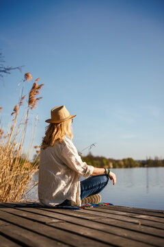 Woman sitting and relaxing on jetty at lake in nature. Tranquil outdoor scene at sunny day. Mindfulness concept