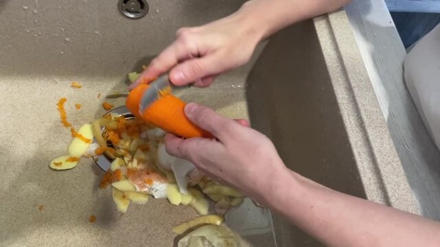hands peeling bright carrot over sink, quick wrist motions with sharp peeler producing curled orange strips, vegetable scraps collected in basin, fresh healthy snack preparation, lively kitchen vibe