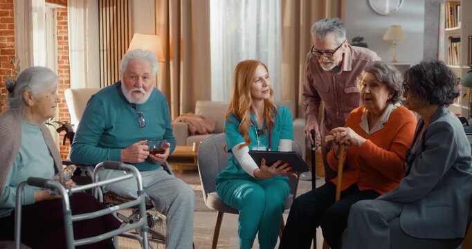 Group of seniors consulting with nurse in nursing home while reviewing information on tablet. Serious communication, care planning and health support in assisted living environment.