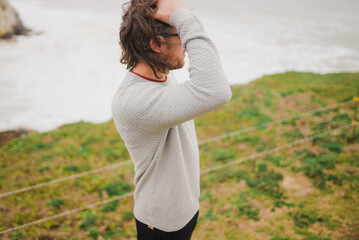 Man stands on grassy cliff, hand in hair © Reuben