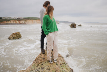 Couple stands on rocky outcrop by crashing sea © Reuben