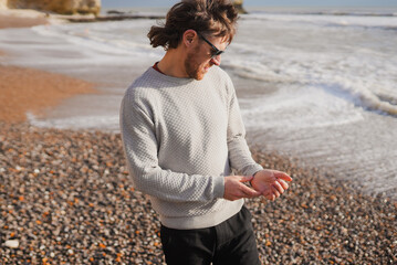 Man stands on pebble beach, gazing at waves © Reuben