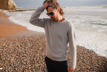 Man stands on pebbled beach, hand on head © Reuben