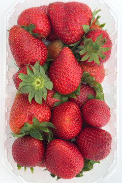 A prominent green calyx rosette stands out among glossy red berries in this full-frame top-down punnet shot &mdash; a clean, detail-rich food photograph with strong retail and commercial appeal.
