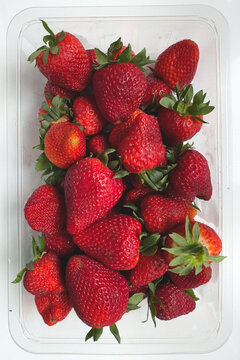 A plastic punnet packed full of ripe strawberries fills the entire frame in this clean overhead shot &mdash; a bold, graphic food flat lay ideal for retail and grocery packaging use.