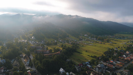 Naklejka premium Mountain village houses nestling in a green valley, surrounded by dense forests and rolling hills, bathed in the warm, golden light of a morning sun
