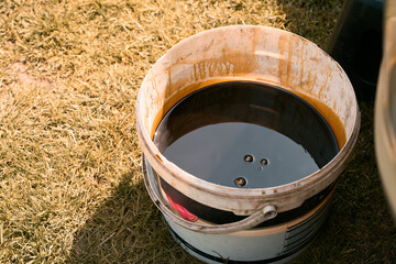 Stained plastic bucket full of used engine oil © AlexGo
