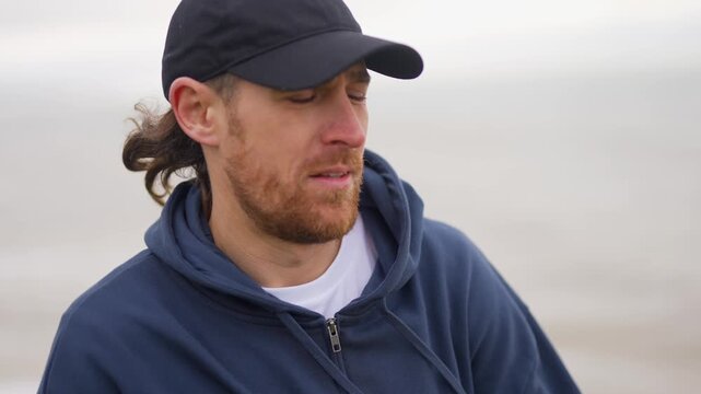 Man wearing baseball cap gazes thoughtfully at the distant ocean shoreline