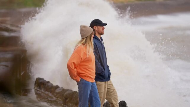 Couple watches powerful waves crash against rocky coastline on a blustery day