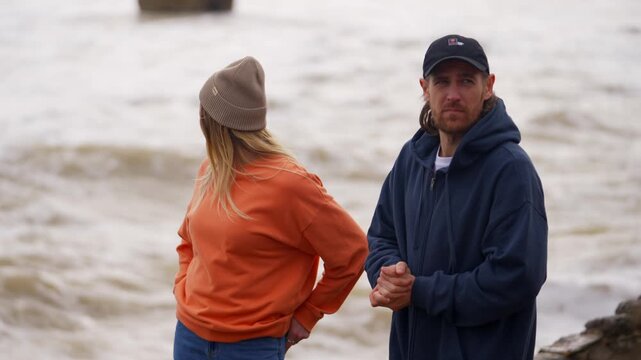 Couple gazes out at choppy water on a cloudy coastal day