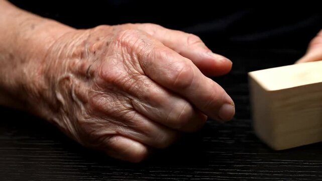 Close-up of elderly hand reaching toward a small wooden block on a surface