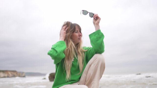 Woman in green sweater sits on beach rocks with ocean backdrop