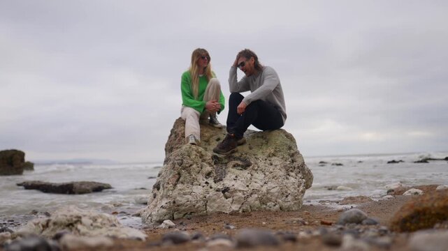 Couple sits on rock overlooking the ocean during a cloudy day