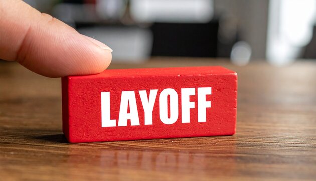 Hand holding a red block with the word Layoff written on it, highlighting job insecurity and economic downturn
