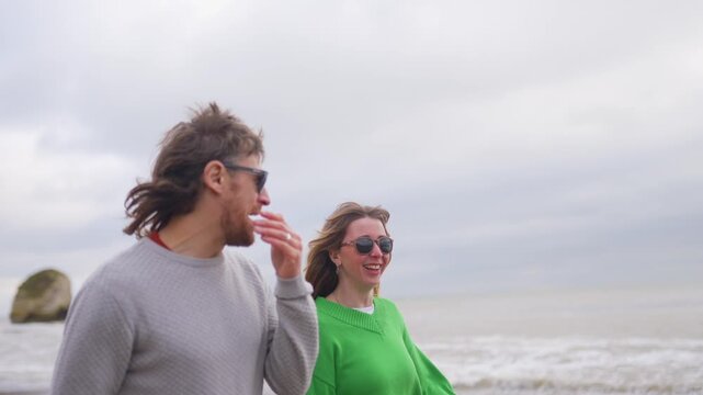 Couple strolls along a windswept beach on an overcast day