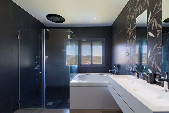 Modern bathroom interior featuring dark gray tiles, white vanity, and glass shower